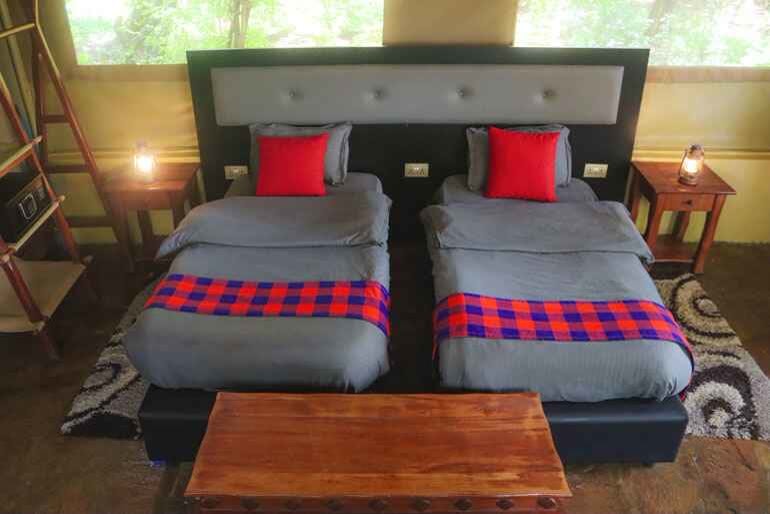 A twin tent with two single beds and red Maasai-check blankets