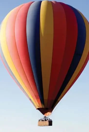Striped hot-air balloon rising into a clear morning sky