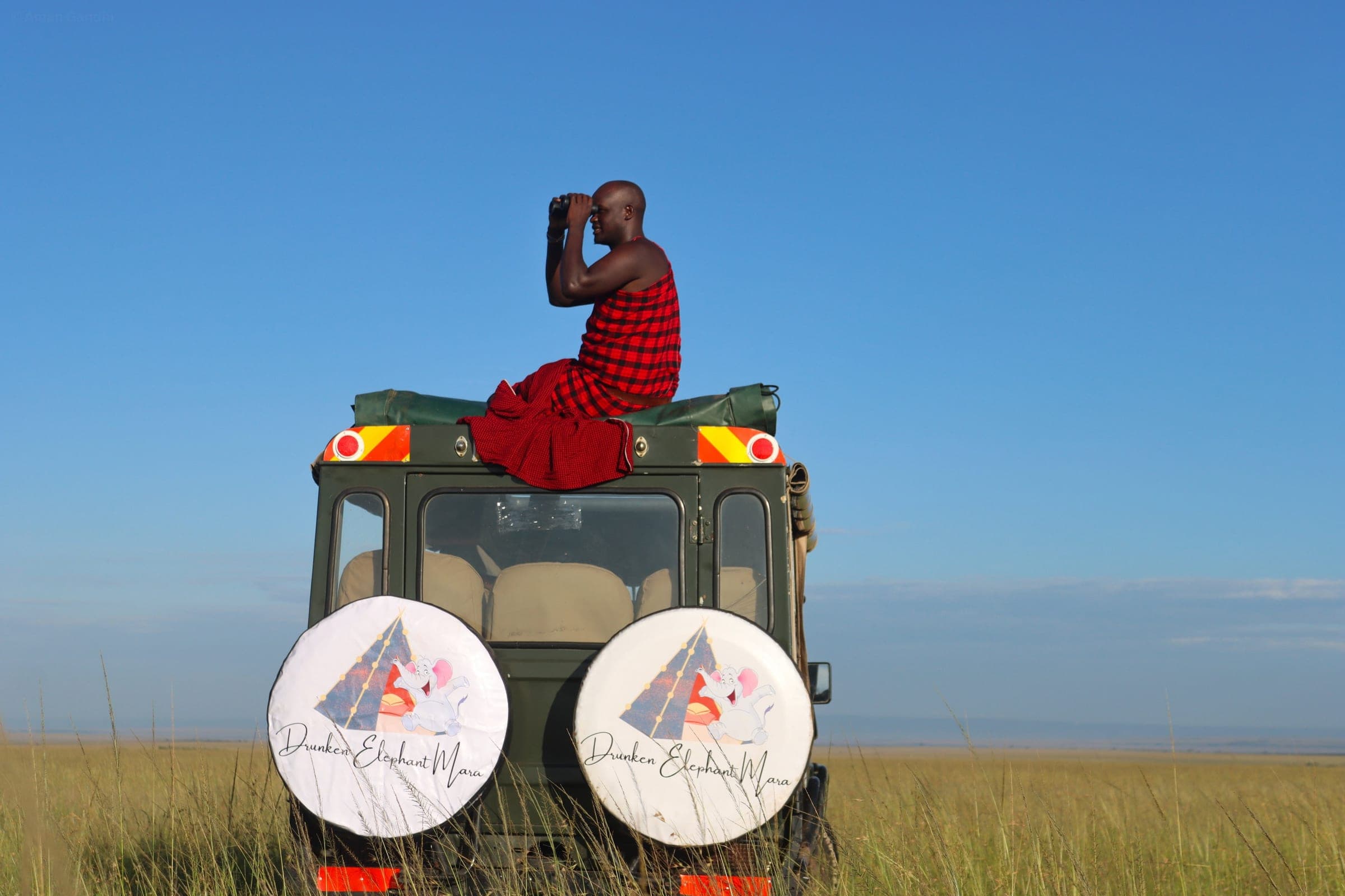 Maasai guide scanning the plains with binoculars from the roof of the camp's game-drive vehicle