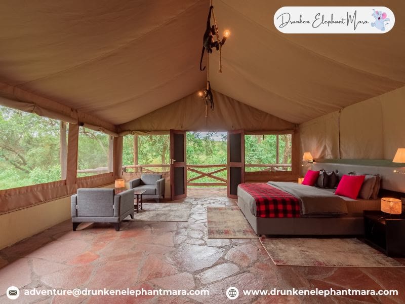 Inside a tent at Drunken Elephant Mara: a double bed with red Maasai-check cushions, armchairs and windows onto the forest
