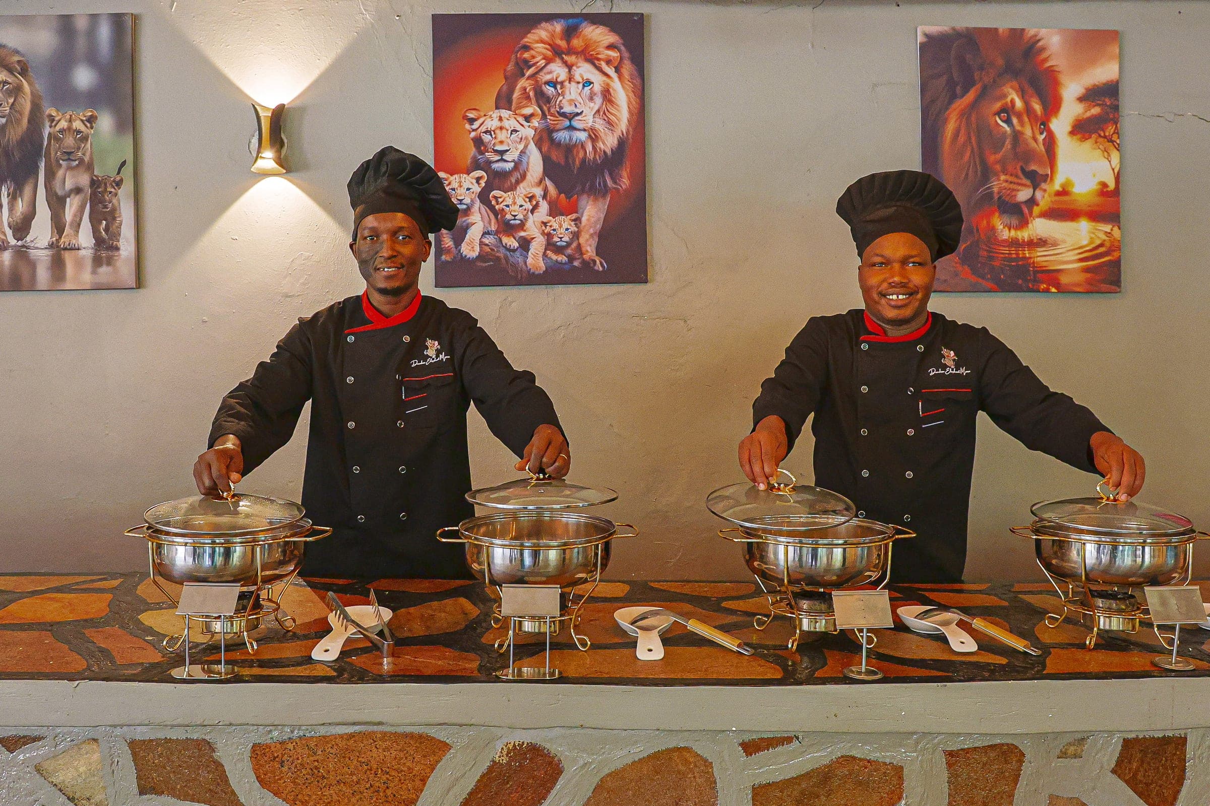 The camp's chefs at the buffet in the mess tent, lifting the chafing-dish lids