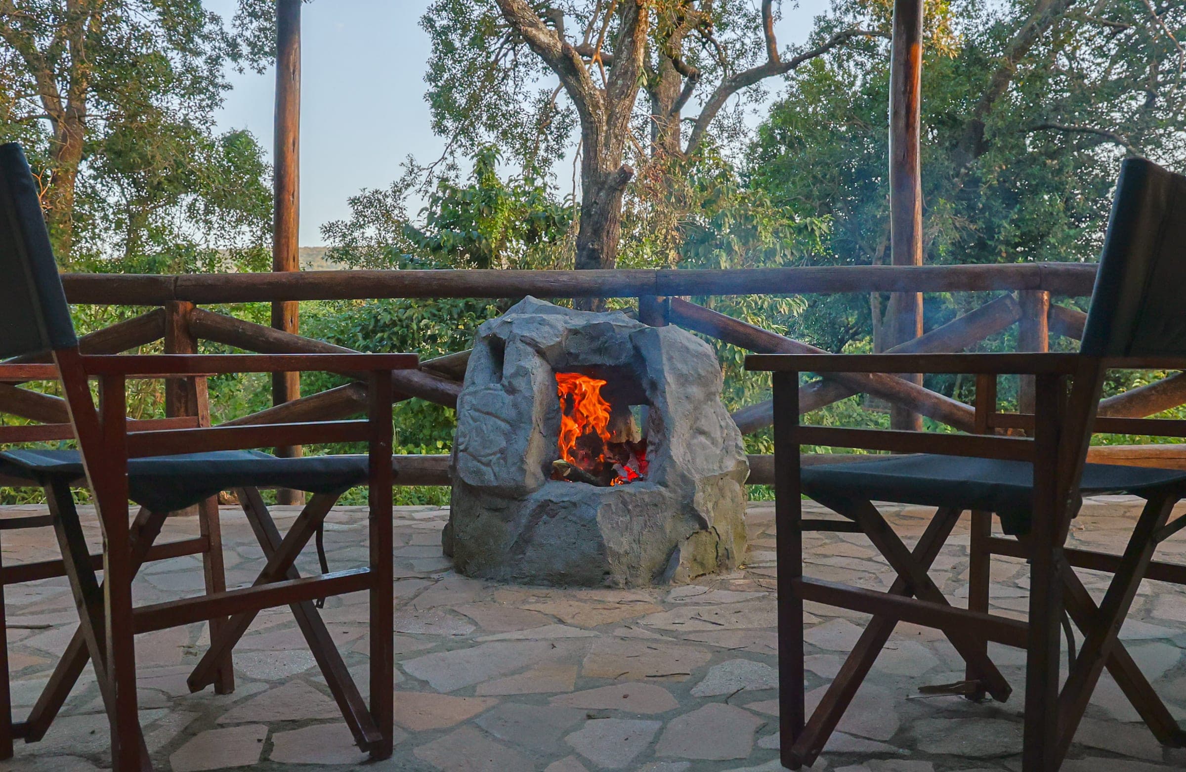 Stone fireplace alight on the Family Tent's private deck, safari chairs either side