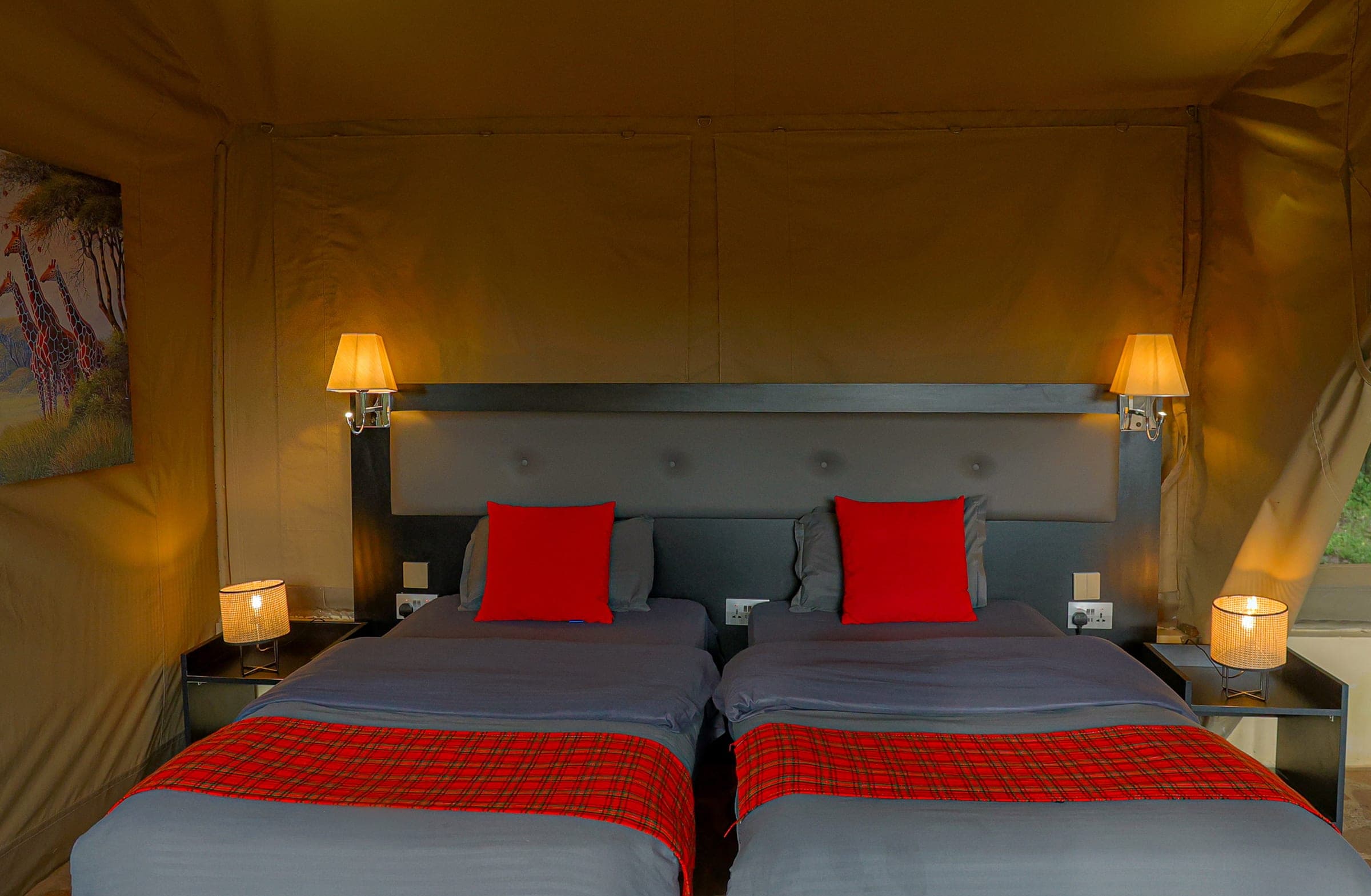 Executive Twin Tent by lamplight: twin beds with red cushions and Maasai-check runners