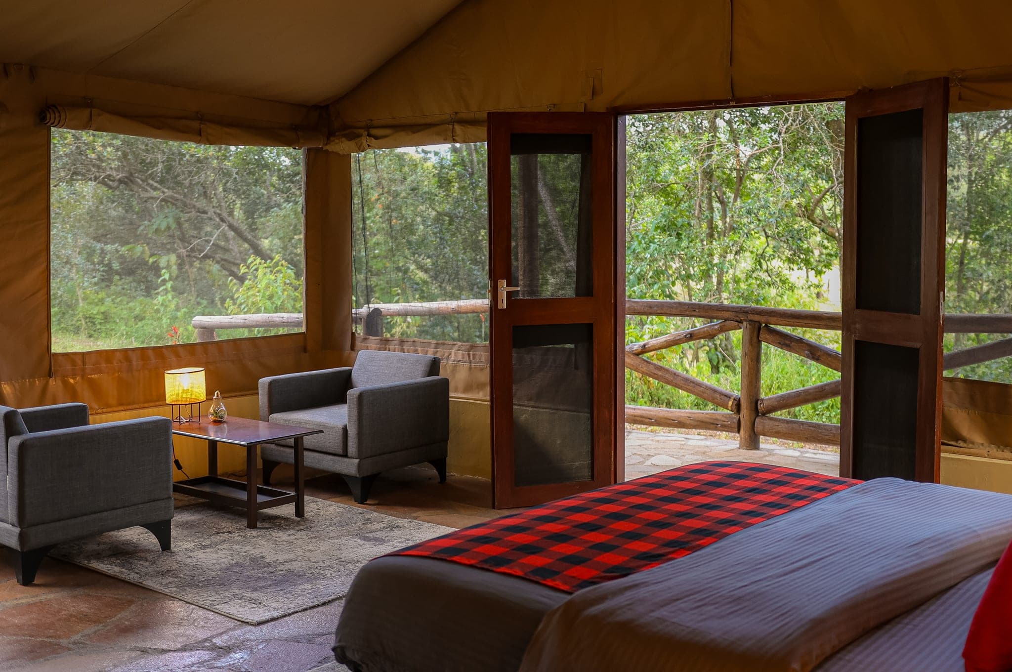 Family Tent with its door open onto the forest deck: armchairs, a Maasai-check blanket and the trees right outside